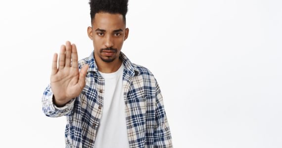 Stop. Serious and determined african american guy extend palm, saying no, rejecting and prohibit smth, stay away, keep social distancing, standing over white background.